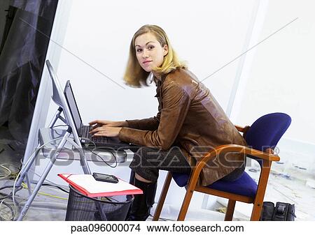 Picture - Woman working on laptop on chair, looking at camera. Fotosearch