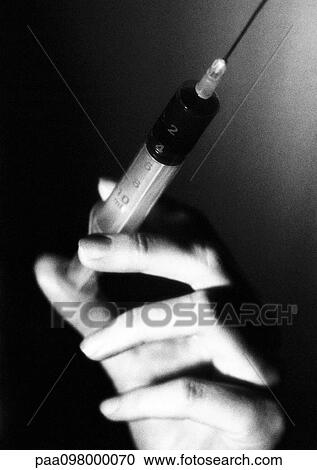 Stock Image - Hand holding syringe, close-up, B&W. Fotosearch