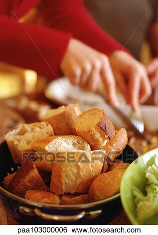 Stock Photograph - Breadbasket, hands holding fork and knife in background, close-up. Fotosearch