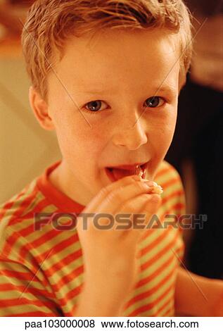 Child putting food in mouth, looking at camera, portrait View Large Photo Image Stock Photo - Child putting food in mouth, looking at camera, portrait. Fotosearch
