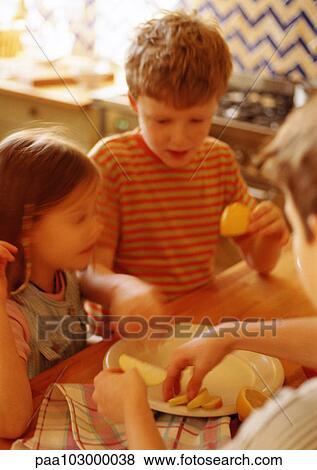 Stock Photo - Children in kitchen putting apple slices on plate, blurred. Fotosearch