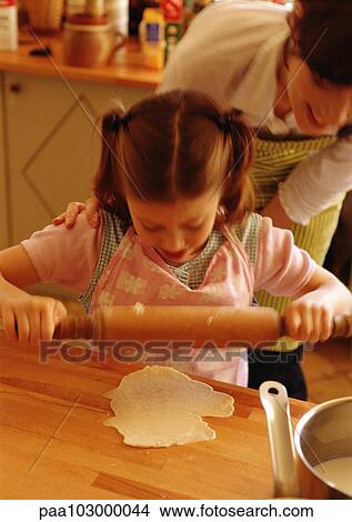 Girl using rolling pin, woman looking over girl's shoulder View Large Photo Image Picture - Girl using rolling pin, woman looking over girl's shoulder. Fotosearch