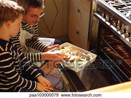 Stock Photo - Man and child putting casserole in oven. Fotosearch