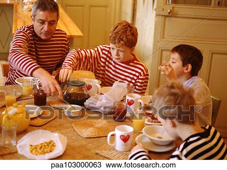 Stock Image - Man and children sitting at table, having breakfast. Fotosearch