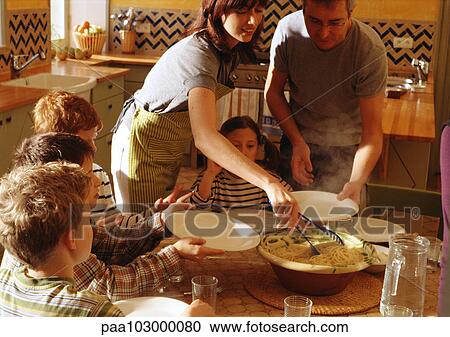Stock Image - Man and woman serving children at table. Fotosearch