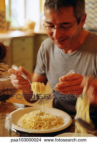 Picture - Man eating spaghetti with fork and spoon, blurred motion. Fotosearch