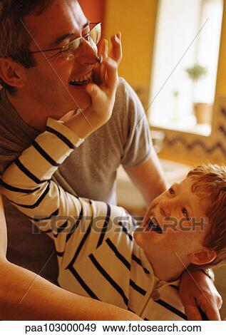 Stock Photo - Man with arms around boy, boy putting hand on man's face, both smiling. Fotosearch