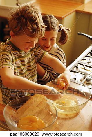 Stock Image - Two children smiling in kitchen with bowl of egg yolks and bowl of egg whites. Fotosearch