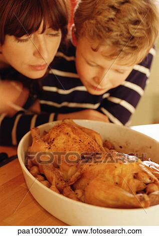 Stock Photo - Woman and child looking at chickens in casserole dish. Fotosearch