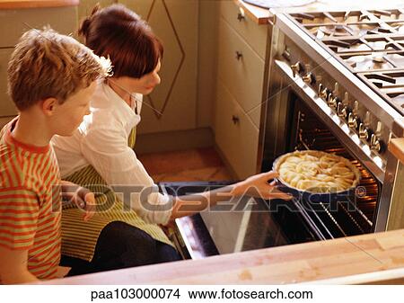 Woman putting pie in oven, child watching View Large Photo Image Picture - Woman putting pie in oven, child watching. Fotosearch