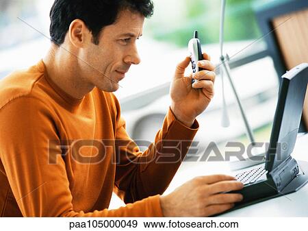 Man holding cell phone, looking at laptop computer View Large Photo Image Stock Photo - Man holding cell phone, looking at laptop computer. Fotosearch