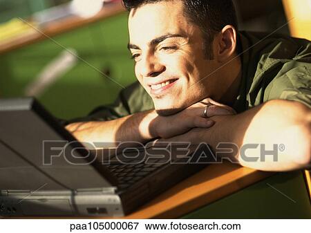 Man leaning on desk looking at laptop computer View Large Photo Image Stock Photo - Man leaning on desk looking at laptop computer. Fotosearch