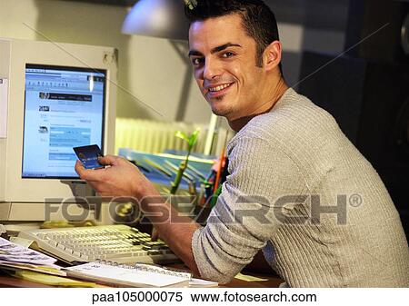 Man sitting at computer, holding credit card, portrait View Large Photo Image Stock Photography - Man sitting at computer, holding credit card, portrait. Fotosearch