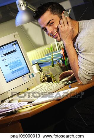 Man sitting at desk with cell phone View Large Photo Image Stock Image - Man sitting at desk with cell phone. Fotosearch