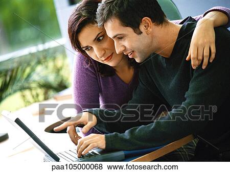 Stock Photo - Man using laptop computer, woman sitting with arm around him. Fotosearch
