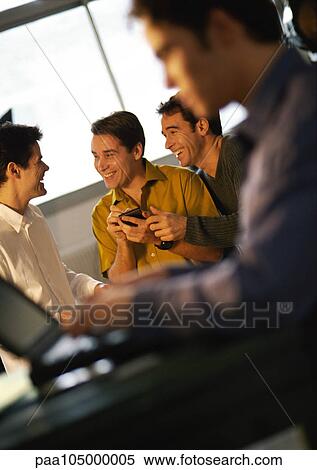 Three men smiling, one holding a hand held computer, fourth man using laptop in foreground View Large Photo Image Stock Photography - Three men smiling, one holding a hand held computer, fourth man using laptop in foreground. Fotosearch