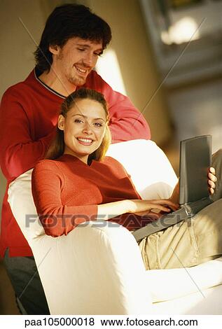 Woman sitting with laptop computer on knees, man looking over her shoulder View Large Photo Image Stock Photo - Woman sitting with laptop computer on knees, man looking over her shoulder. Fotosearch