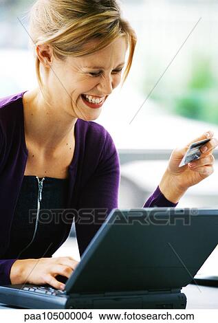 Woman using laptop computer and holding credit card, laughing View Large Photo Image Picture - Woman using laptop computer and holding credit card, laughing. Fotosearch