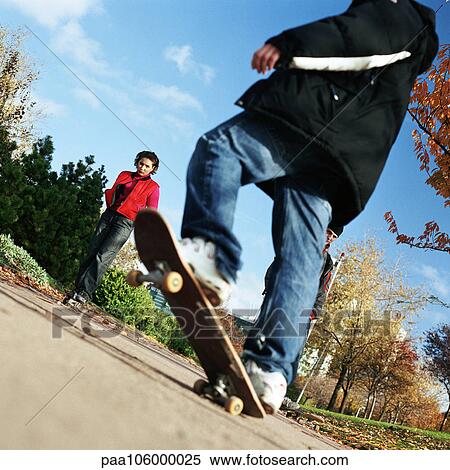 Stock Photography - Person on skateboard, young woman in background, low angle view. Fotosearch