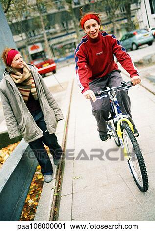 Stock Image - Two young people on sidewalk, one on bike. Fotosearch