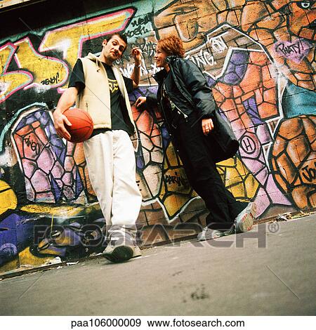 Stock Photo - Young man and woman leaning against graffitied wall. Fotosearch