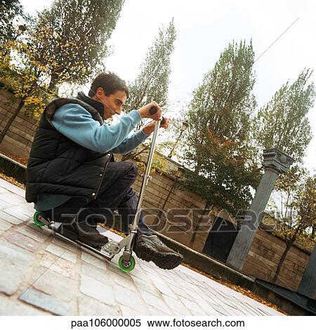 Young man sitting on push scooter, side view View Large Photo Image Stock Photography - Young man sitting on push scooter, side view. Fotosearch