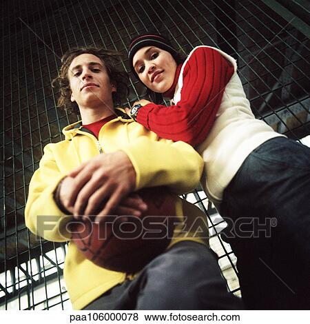 Stock Photo - Young man with basketball, young woman leaning on his shoulder, low angle view. Fotosearch