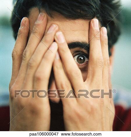 Young man with hands over face, looking through fingers with one eye, close-up View Large Photo Image Stock Photo - Young man with hands over face, looking through fingers with one eye, close-up. Fotosearch