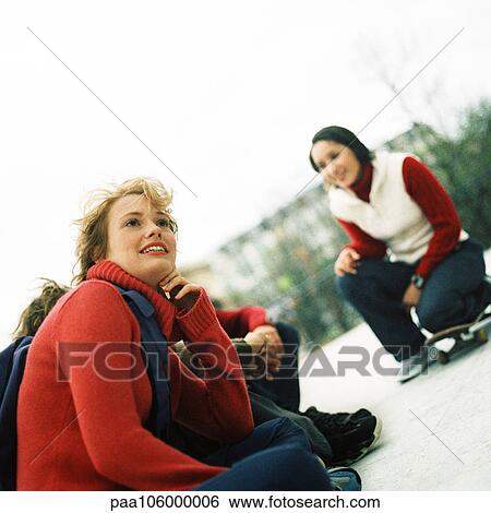 Stock Photograph - Young people outdoors, one with knee on skateboard. Fotosearch