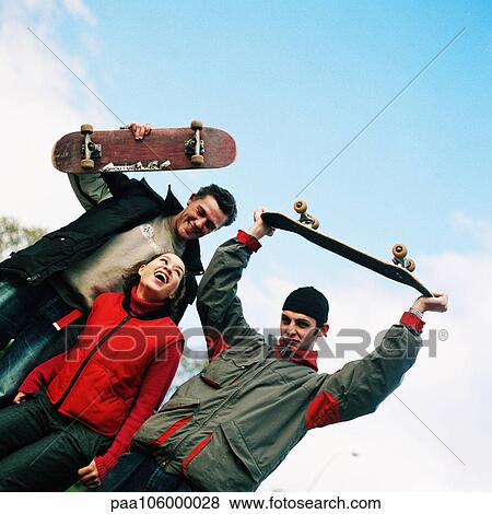 Young woman between two young men holding skateboards, portrait View Large Photo Image Stock Photo - Young woman between two young men holding skateboards, portrait. Fotosearch