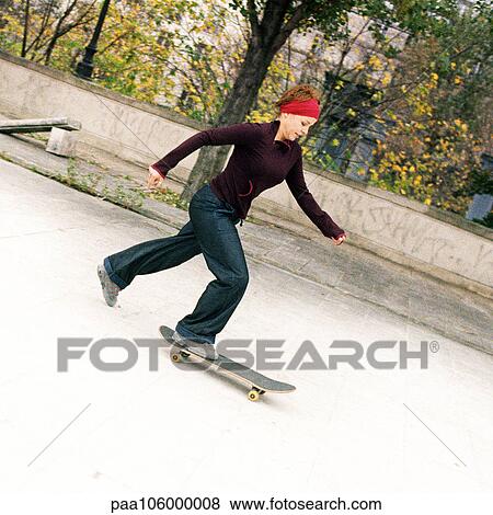 Stock Photo - Young woman skateboarding, side view. Fotosearch