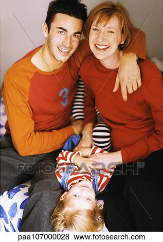 Stock Photo - Child lying down between couple, portrait. Fotosearch