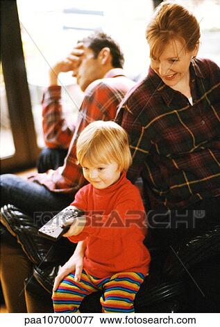 Stock Photo - Child sitting in front of parents, pointing remote control. Fotosearch