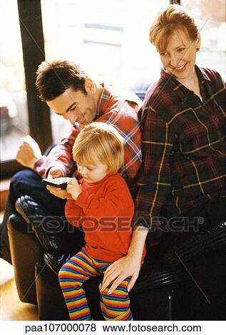 Child sitting in front of parents, holding remote control View Large Photo Image Stock Photo - Child sitting in front of parents, holding remote control. Fotosearch