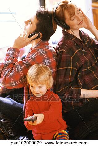 Stock Photo - Child sitting in front of parents, pointing remote control. Fotosearch