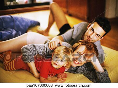 Stock Image - Couple and child lying on bed, portrait. Fotosearch