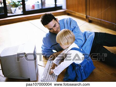 Man lying on floor, child in front of computer View Large Photo Image Picture - Man lying on floor, child in front of computer. Fotosearch
