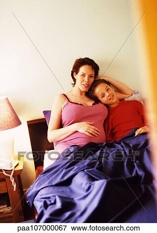 Pregnant woman and child sitting in bed together View Large Photo Image Stock Photo - Pregnant woman and child sitting in bed together. Fotosearch