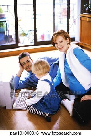 Stock Photograph - Pregnant woman and man on floor with child touching computer keyboard. Fotosearch