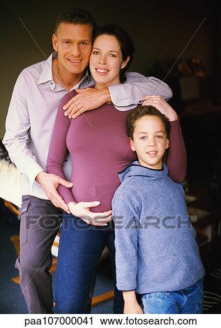 Stock Image - Pregnant woman and man standing with child, smiling, portrait. Fotosearch