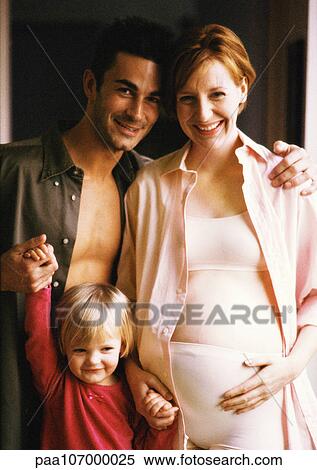 Stock Photography - Pregnant woman and man standing with child, smiling, portrait. Fotosearch