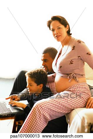 Stock Image - Pregnant woman sitting with man and child, child using laptop computer. Fotosearch