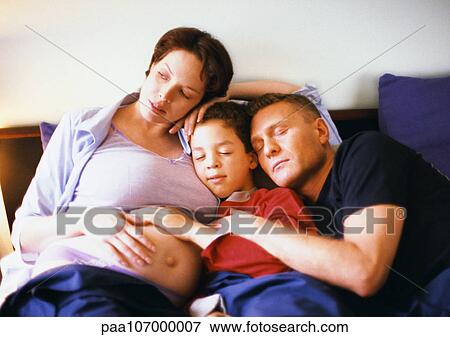 Stock Photo - Pregnant woman sitting with man and child in bed. Fotosearch