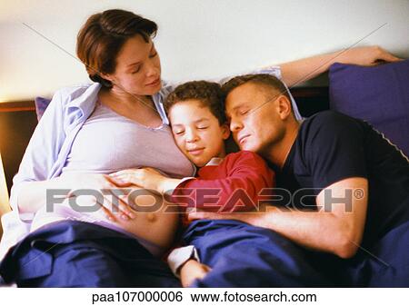 Stock Photograph - Pregnant woman sitting with man and child in bed. Fotosearch