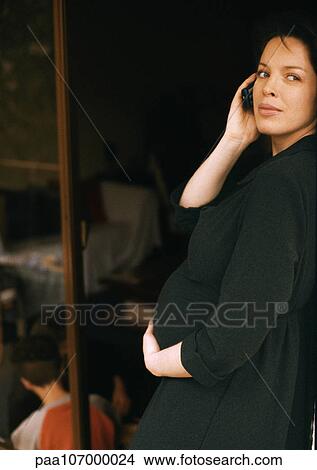 Pregnant woman standing, using cell phone, child sitting on floor in background View Large Photo Image Picture - Pregnant woman standing, using cell phone, child sitting on floor in background. Fotosearch