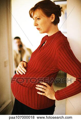 Stock Photo - Pregnant woman standing with hand on stomach, side view. Fotosearch