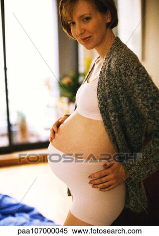 Stock Photography - Pregnant woman standing with hand on stomach. Fotosearch