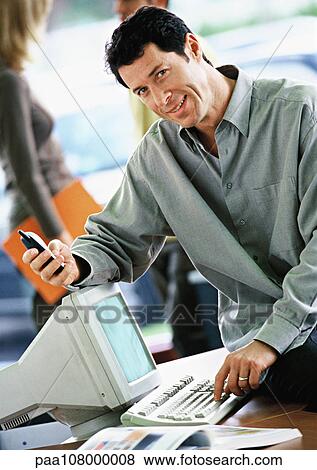 Stock Photo - Businessman sitting on desk with cell phone. Fotosearch