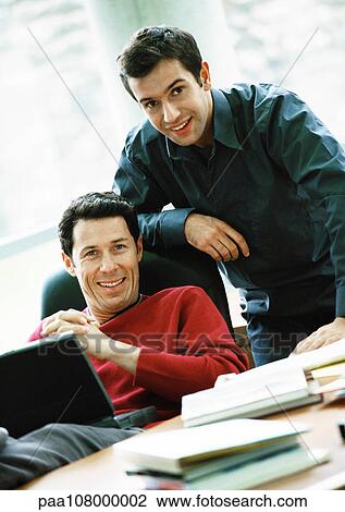 Stock Image - Businessmen smiling, one with laptop on lap, portrait. Fotosearch