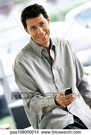 Picture - Man holding cell phone in front of him, smiling, waist up.. Fotosearch